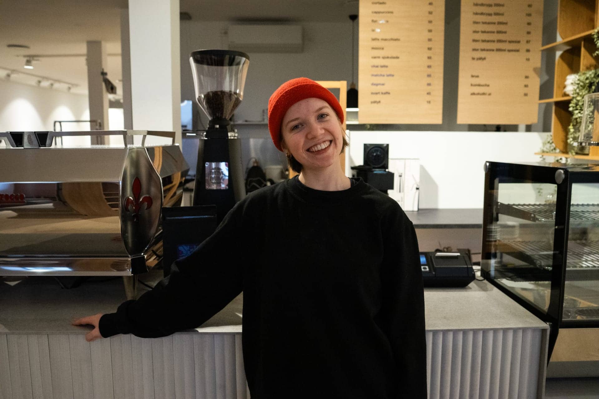 Barista bak disken ved espressomaskinen, med menyen i bakgrunnen