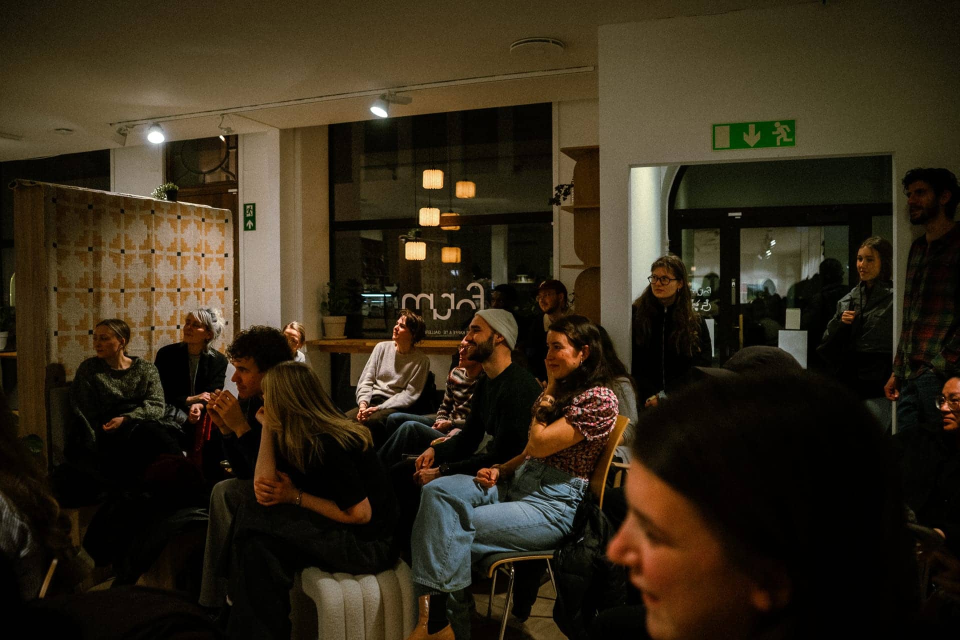 Kveldslys i kafeen: gjester vendt mot scenen, Forum-merket i vinduet